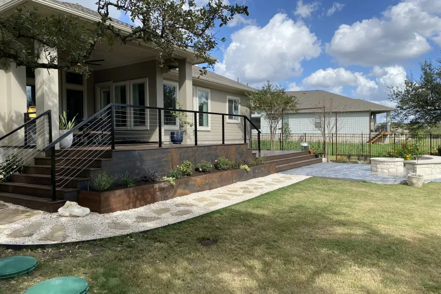 Raised deck with corten steel skirting and cable railing leading down to a stone patio and fire pit in Austin, TX