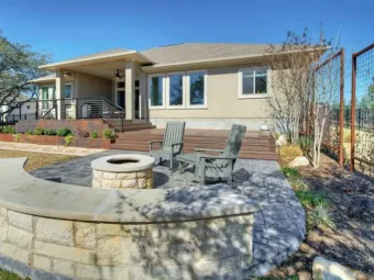 Backyard patio with a curved stone fire pit and built-in bench seating leading up to a wood deck
