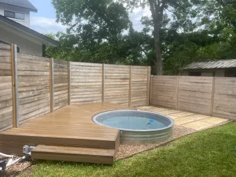 Wide view of a wood deck, built-in stock-tank pool, and cedar privacy fence in an Austin backyard