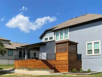 Wide exterior view of an Austin home with a raised cable-rail deck, stairs, and paver patio