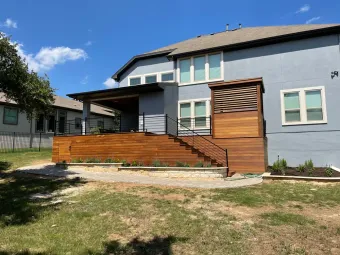 Two-story Austin home with a raised cable-rail deck, stairs, and paver patio with landscaped planting beds