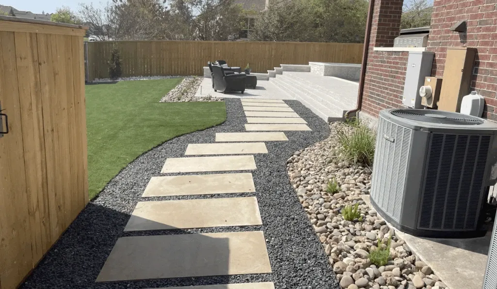 Paver walkway installation through an Austin backyard with turf and river rock