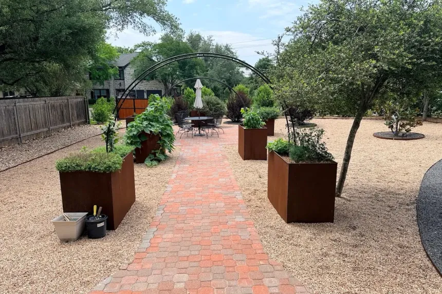 Brick paver path through an Austin garden design with corten steel planter boxes, a herb garden, and a shade arbor