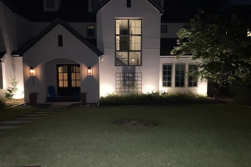 Austin home at night with landscape uplighting on the facade, trellis, and entryway sconces illuminating the front door