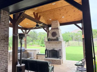 Covered outdoor living pavilion with stone fireplace, seating, and built-in kitchen counter in Austin, TX