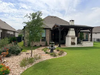Backyard view of an Austin home with a covered outdoor living pavilion, stone fireplace, and garden fountain