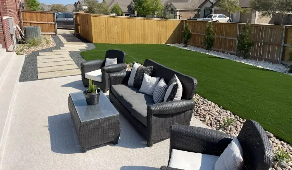 Modern outdoor seating setup in a pet-friendly backyard with artificial turf, stone edging, and privacy fence.