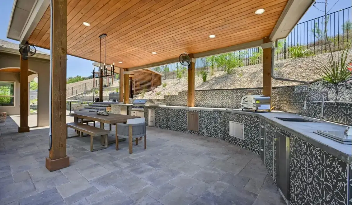 Outdoor kitchen installation with covered structure and custom tile design in Austin, featuring a spacious cooking area, dining table, and ample counter space.