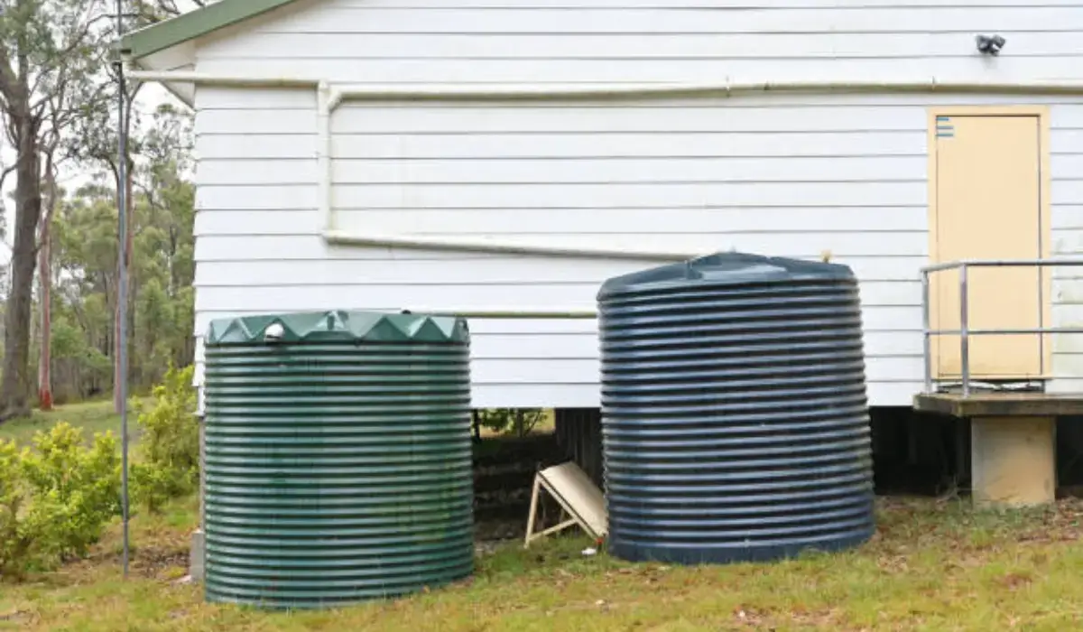 Two large rainwater collection systems installed beside a white house for sustainable landscape irrigation in Austin.