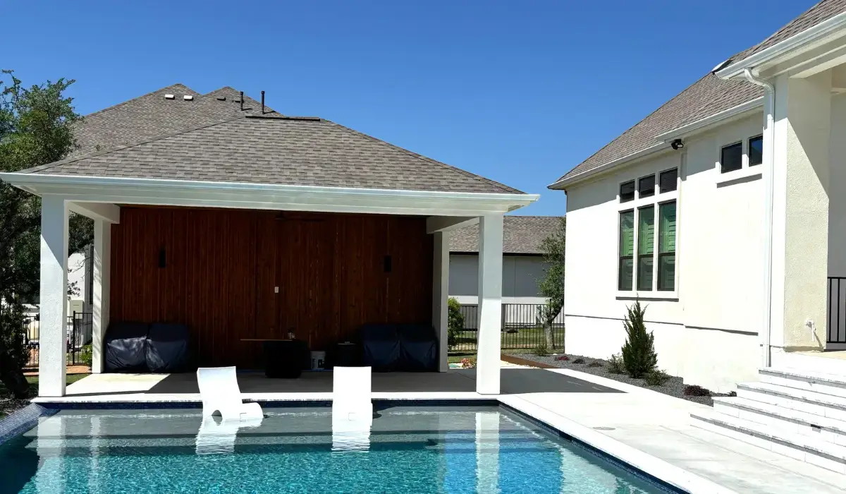 Covered veranda living space with seating area facing a modern backyard pool under blue sky.