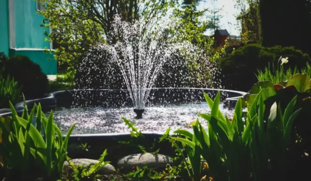 Custom water feature with a central fountain spraying into a round pond surrounded by garden plants.