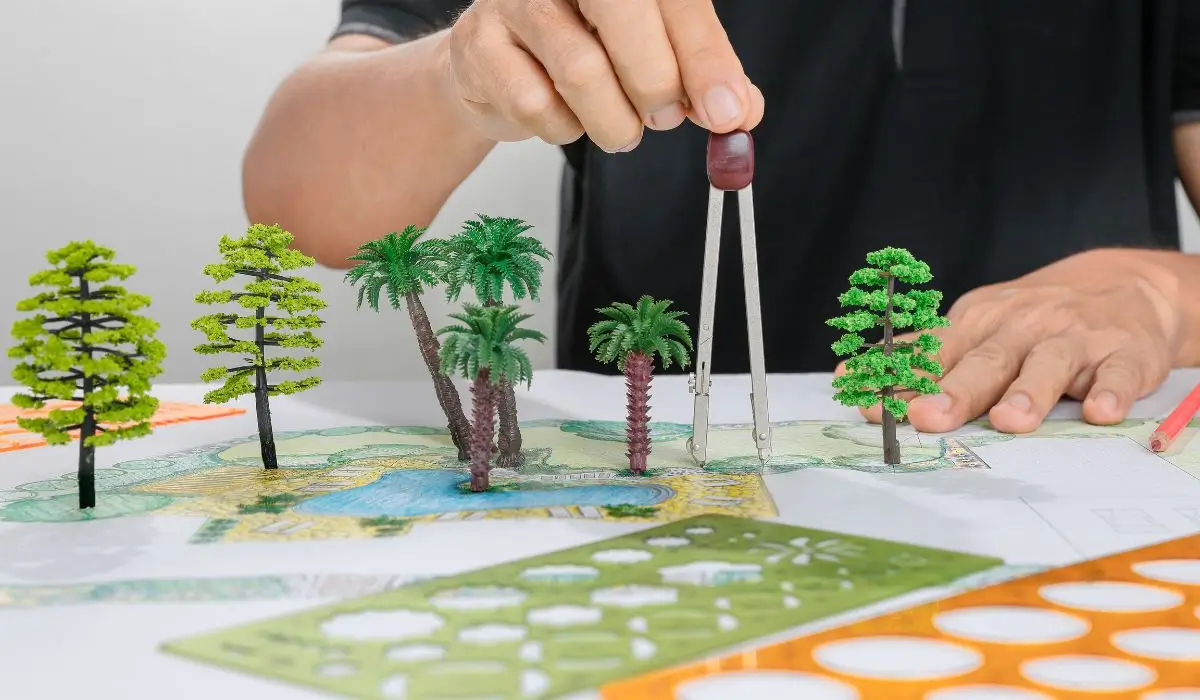 Close-up of a landscape architect designing an outdoor layout with scaled trees and site plan tools.