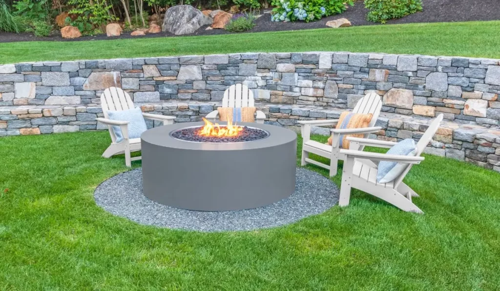 Modern fire pit landscaping with sleek stone wall, Adirondack chairs, and green lawn for stylish outdoor living.