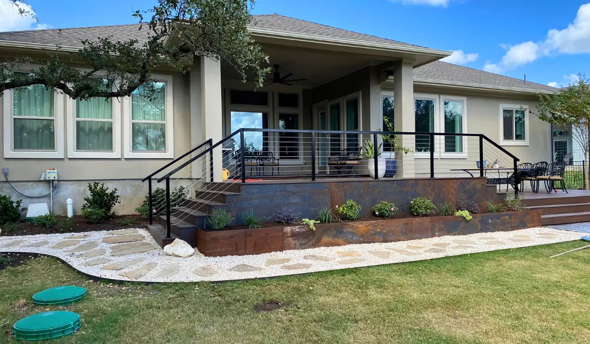 Completed landscape renovation project in Austin showing a modern backyard with a raised patio, stone walkway, and newly planted greenery.