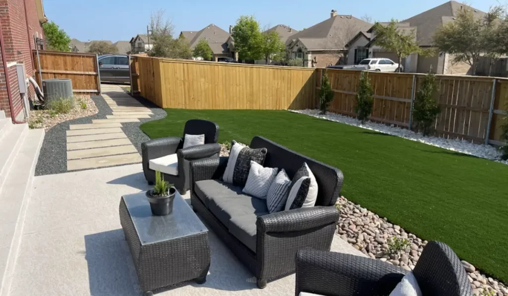 Small backyard design featuring turf lawn, paver walkway, modern patio seating, and decorative stone borders.