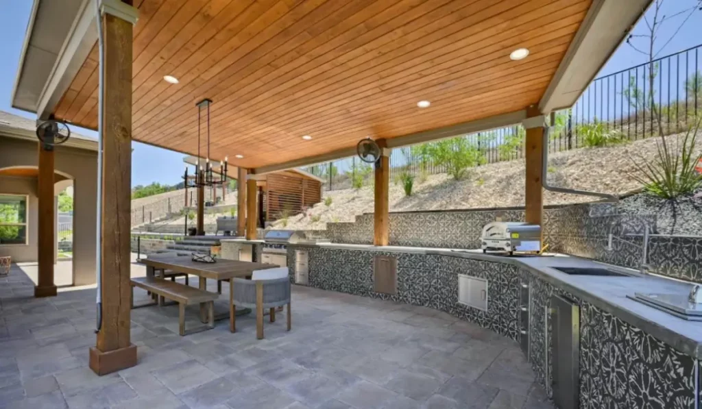 Outdoor living features with custom covered patio, full outdoor kitchen, dining area, and weather-ready design.
